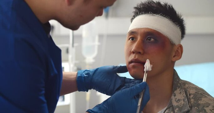 Close up of doctor cleaning wound on face of asian soldier in army hospital