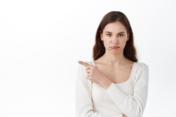 Blame, accusation. Displeased young woman pointing index finger aside, showing bad promo, sulking...