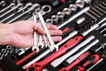 Fototapeta premium Tool store. Closeup of male hand holding wrenches. Auto repair kit in toolbox. Repairman instruments set. Inside the toolbox there are black-red wrenches, spanners and different nozzles. Closeup.
