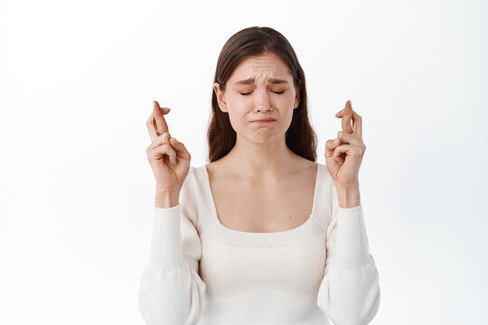 Portrait of hopeful brunette girl making wish crossed fingers for good luck, close eyes and putting all effort into pray, pleading for dream come true, anticipating over white background