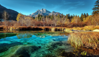 Amazing nature scenery. Zelenci lake in Slovenia. Beautiful azure lake with mountains and majestic mount in the background. Panorama autumn landscape photo. Concept of an ideal resting place.
