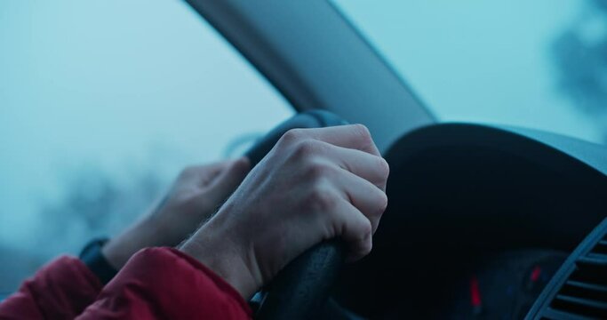 Cinematic inspiring blue palette shot of man in red puffy jacket drive camper van or delivery truck during bad storm winter weather. Man drives car, hold hands on steering wheel