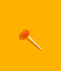 Orange and yellow hard candy lollipop on stick laying on orange background top view with trendy...