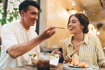 Cheerful man feeding girlfriend in cafe