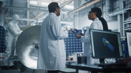 Engineer and Technician Talk, Use Tablet Computer while Working on Satellite Construction