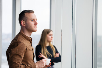 Stylish young couple in love in front of large panoramic windows. A young woman and a man are standing at a large window with coffee. Selective focus