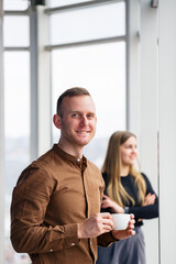 Stylish young couple in love in front of large panoramic windows. A young woman and a man are standing at a large window with coffee. Selective focus