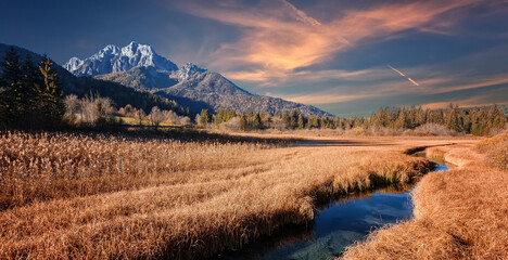 Fantastic nature scenery during sunset. Amazing view on mountains valley with river, grassy meadow and majestic rocky peak under sunlight, on th beckground. Stunning nature background.