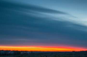 Panorama of dawn fire in the sky above the natural pasture. Golden red clouds just before sunrise. Picturesque landscape at sunrise. Beauty in nature