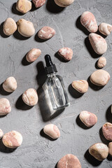 Skin care essence oil dropper in glass bottle near to pebbles