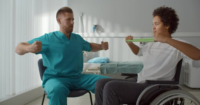 Disabled young afro woman doing exercises in hospital with doctor