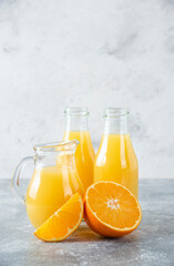 A glass pitcher of juice with fresh orange fruits on stone background