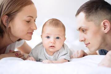 Smiling mother and father with a newborn baby in bed