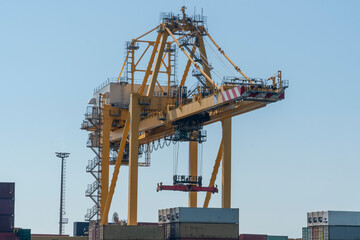 Worldwide shipping and cargo concept:  View on yellow crane lift standing at a dockyard to move containers. Construction equipment for logistics. Global import export crises due to Covid-19 pandemic
