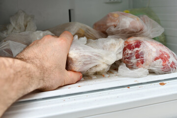 A man pulls frozen vegetables out of the freezer. A man takes corn from the fridge. Plastic containers with frozen meat, vegetables and fruits.
