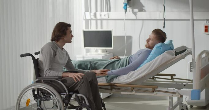 Young man in wheelchair visiting friend in hospital ward