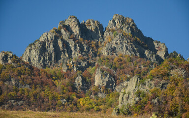 The eroded calcareous cliff of Cozia Mountains raising above a pasture. Autumn season, the beech forest got colored leaves. Carpathia, Romania 