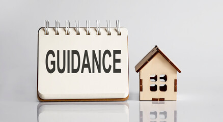 GUIDANCE words written in an office notebook with wooden house. Financial Business concept.