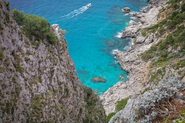 Amazing cliffs in Capri island overlooking the mediterranean sea. Beautiful landscape with blue sea in summer sunny day with a yellow  fishing boat in background, Capri Island, Tyrrhenian sea, Italy