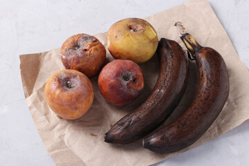 Spoiled rotten foods with mold: apples and banana on gray background