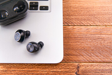 Overhead shot of wireless headphones or earphones with bluetooth connection with its storage box and charging on a laptop. Copy space