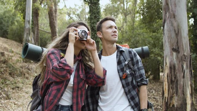 Hikers with photo camera taking pictures of forest landscape, while walking on path, enjoying outdoor vacation and healthy recreation. Adventure travel concept