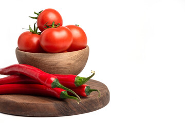 A wooden bowl full of fresh red juicy tomatoes with red hot chili peppers