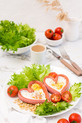 Love breakfast. Fried eggs in heart shaped sausages, lettuce and cherry tomatoes on a plate and a cup of coffee on the table. Vertical view