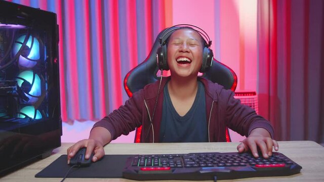 Asian Boy Wearing Headphones Playing Video Game, Laughing While Playing Video Game
