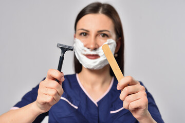 Woman beautician with shaving foam showing depilation spatula and disposable razor