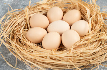 Bunch of raw eggs with bird nest on marble surface