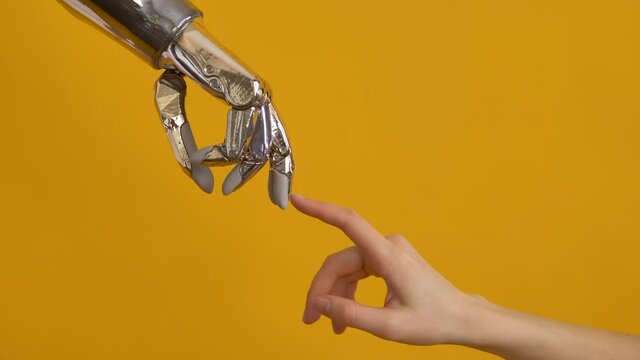 Young woman touches finger of person using contemporary shiny metal bionic arm against bright yellow background close view