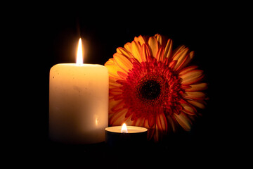 due candele accese e una gerbera su sfondo nero, vista frontale. condoglianze
