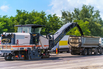 Big special machinery pours fresh asphalt out to smaller truck. New road construction. Selective...