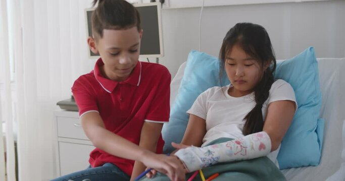 Mixed-race preteen boy visiting asian girl friend in hospital painting hand cast together