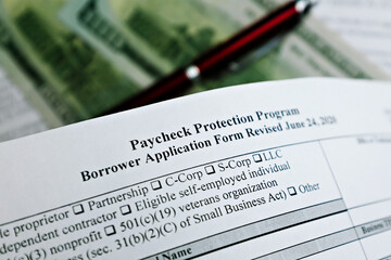 Obraz premium selective focus photo of paycheck protection program borrower application form revised, on a background of dollar bills and a pen