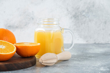 A glass pitcher of juice with fresh orange fruits on stone background