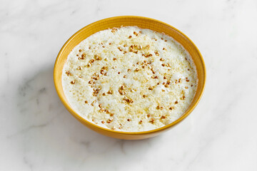 Buckwheat porridge cooked on milk in a bright yellow bowl on a light marble background