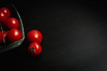 Red tomatoes in glass bowl on dark background