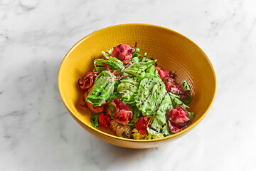 Fresh salad with medium-rare roast beef slices, with cherry tomatoes in a yellow bowl on a white marble table