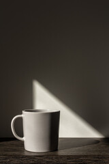 Beige mug in bright sunlight on wooden table. Gray background with shadow and graphical triangular sun spot light. Minimal style mockup with copy space. Hard light and shadows concept.