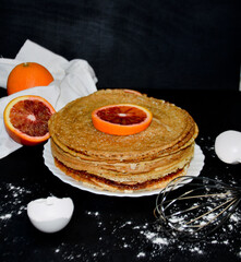 pancakes in a plate next to an orange egg shell on a black background selective focus