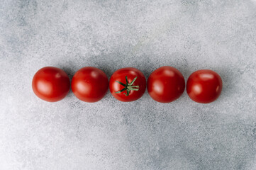 Line of red tomatoes on gray background