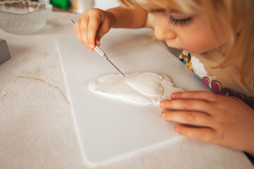 The hands of a small child who rolls out the clay to create a gift, a surprise for relatives and families. Child development, hobbies, clay hobby. Made by hands. Cozy home atmosphere.