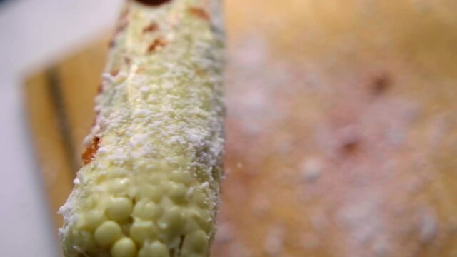 Hand sprinkling chili powder on corn above wooden cutting board