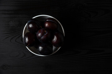 Black plums in a white ceramic saucer