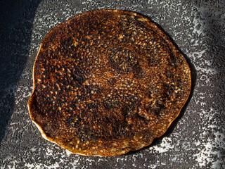 Fototapeta premium A disproportionate golden pancake on a black background of a textured table in the sunlight. The concept of the spring pagan Slavic holiday.