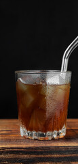 Iced coffee in a low glass on a black background. Drops on a glass. Wooden plank. Vertical orientation. Selective focus on the front of the glass. Copy space