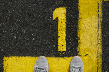 Close up, Men with grey sneker and jeans stand on the number 1, sign on the asphalt, yellow painted number and lines on dark street, space for text
