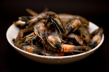 Raw shrimps in a white plate on a black background.